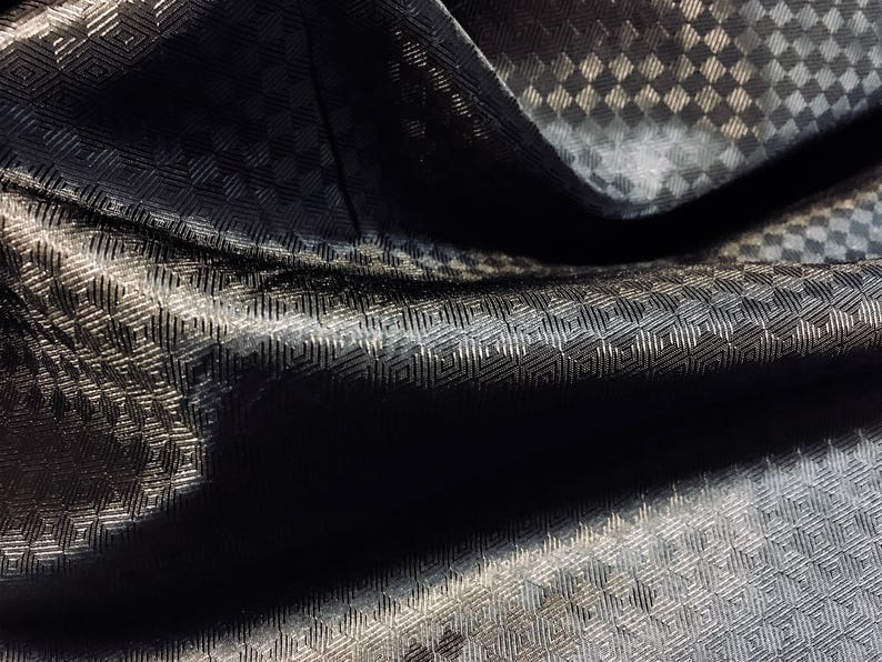 May include: Black fabric with a subtle geometric pattern. The fabric is folded and has a textured surface.