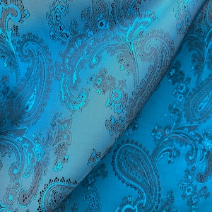 Pode incluir: Tecido turquesa com um padrão paisley preto. O tecido está dobrado ao meio, mostrando o padrão em ambos os lados.