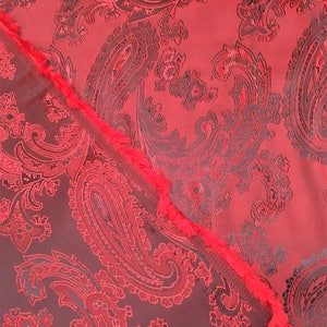 May include: Red paisley fabric with a black and red pattern. The fabric has a textured surface and a fringed edge.