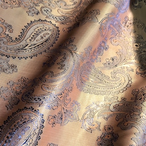 May include: A close-up of a gold fabric with a paisley pattern. The fabric has a subtle sheen and a soft texture.