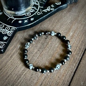 May include: Black and white beaded bracelet with silver accents. The beads are round and have a speckled pattern.