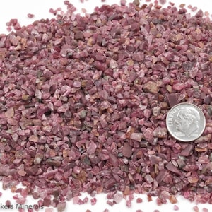 May include: A close-up of a pile of small, pink ruby chips. A US dime is included for scale.