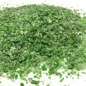 May include: A close-up of a pile of green, crushed glass. The glass is small and irregular in shape, and it has a slightly iridescent sheen.