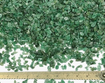 Könnte beinhalten: Eine Ansammlung kleiner, unregelmäßiger, durchscheinender grüner Mineralfragmente, die auf einer Fläche verstreut sind. Ein Metalllineal liegt horizontal am unteren Rand und zeigt Maße in Zentimetern von 1 bis 10. Der Text Makers Minerals ist sichtbar.