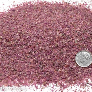 Puede incluir: Un montón de piedras preciosas rosas y moradas, pequeñas y trituradas. Una moneda de diez centavos estadounidense está junto a las piedras preciosas para comparar el tamaño. Las piedras preciosas son una mezcla de colores, incluyendo rosa, morado y algo de verde.