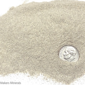 May include: A close-up of a pile of light gray sand with a US dime coin for scale.