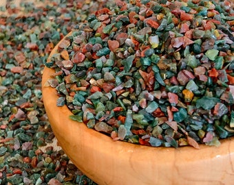 Può includere: Una ciotola di legno piena di piccole pietre colorate e levigate. Le pietre sono un mix di rosso, verde e marrone.