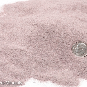 May include: A close-up of a pile of light pink sand with a US dime coin on top. The coin is dated 2016.