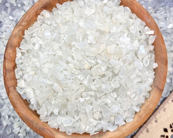 Può includere: Una ciotola di legno piena di pezzi di cristalli di selenite bianchi, traslucidi e di forma irregolare.