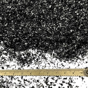 Puede incluir: Purpurina de vidrio negro triturado con una regla para la escala. La purpurina tiene aproximadamente 3 mm de tamaño.