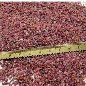Könnte beinhalten: Ein Haufen kleiner, unregelmäßig geformter, rot-violetter Edelsteine. Ein goldfarbenes Lineal liegt am unteren Bildrand, mit Maßen in Zentimetern. Die Edelsteine scheinen roh oder unpoliert zu sein, mit verschiedenen Rot- und Violetttönen.