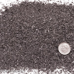 May include: A close-up view of a pile of black volcanic sand. A US dime coin is placed on top of the sand for scale.