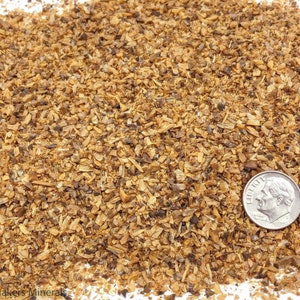 May include: Close-up of a pile of brown and tan wood chips. A US dime coin is placed on top of the wood chips for scale.