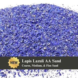 May include: A pile of crushed Lapis Lazuli AA sand in various sizes, from coarse to fine. The sand is a deep blue color with flecks of gold and white. The image includes a gold "NEW" sticker and text that reads "Lapis Lazuli AA Sand".