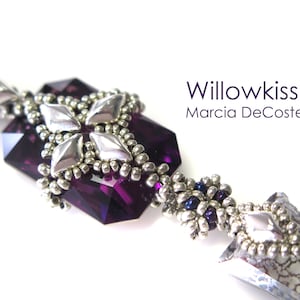May include: A purple crystal pendant with silver beading and a geometric design. The pendant is attached to a silver chain with a silver bead at the end. The pendant is labelled "Willowkiss Marcia DeCoster".