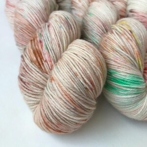 May include: A skein of yarn in a cream base with splashes of peach, orange, green, and yellow.