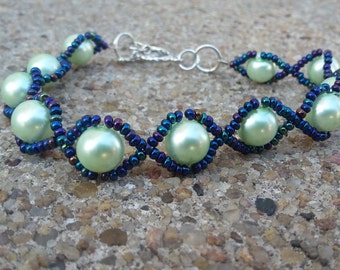 May include: A delicate bracelet with a woven design featuring alternating light green and dark blue beads.