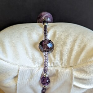 May include: A purple and silver beaded bracelet with a large faceted purple bead in the center.