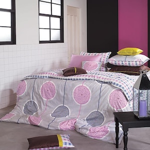 May include: A bed with a gray comforter featuring a pink and gray circular design. The bed is adorned with various pillows in shades of pink, brown, and yellow. The room has a modern aesthetic with black framed windows and a black accent wall.