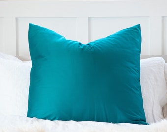 May include: A teal blue pillow on a white bed with a white fluffy blanket.