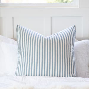 May include: A blue and white striped pillow on a white bed. The pillow is made of a soft, comfortable fabric and has a classic striped pattern.
