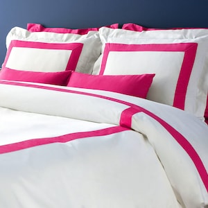 May include: White bedding with a pink border. The bedding is made of a soft, comfortable material and features a simple, elegant design.