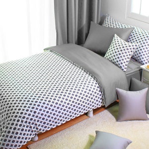 May include: A bed with a gray and white geometric patterned duvet cover and matching pillowcases. The bed is made up with gray pillows and a gray bed skirt. The bed is on a white rug.