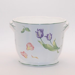 May include: White ceramic planter with a scalloped rim and two small handles. The planter is decorated with purple tulips, green leaves, and pink and yellow petals. A green trim accents the rim and base.