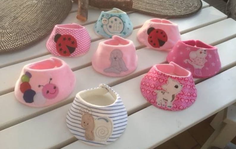 May include: A collection of eight pink and blue baby bibs with various embroidered designs, including ladybugs, snails, hearts, and animals.