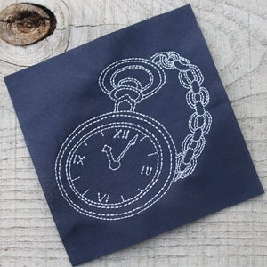 May include: White embroidered pocket watch with Roman numerals on a dark blue fabric background.