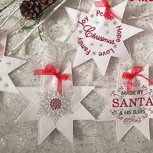 Puede incluir: Cinco estrellas de fieltro blanco con lazos de cinta roja. Las estrellas están decoradas con purpurina plateada y bordadas con texto navideño, incluyendo "Love, Joy, Peace, Hope, Family, Christmas" y "Made by Santa & His Elves".