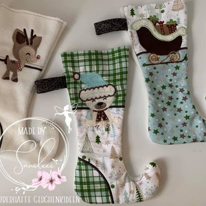 Peut inclure: Trois chaussettes de Noël avec des motifs différents. Une chaussette est blanche avec un renne, une autre est bleue avec des étoiles et un traîneau, et la dernière est verte et blanche avec un motif à carreaux et un ours.