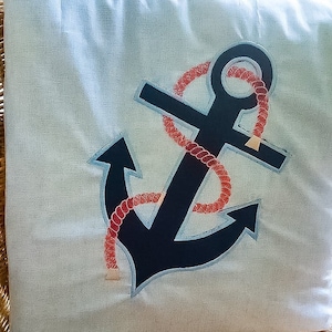 May include: A blue and white throw pillow with an embroidered anchor and red rope design.