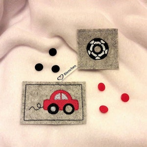 May include: Three felt patches with embroidered designs. One patch features a red car with a white windshield and wheels. Another patch features a black and white circle design. The third patch has the word "Bienchen" in white with a heart symbol.