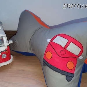 Könnte beinhalten: Ein graues und orangefarbenes Kissen mit einem roten gestickten Volkswagen-Bus-Design. Der Bus hat weiße Fenster und ein Herz vorne.