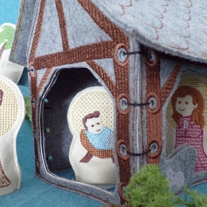 Könnte beinhalten: Eine Filz-Krippe mit einem braunen Holzstall, einem Hirten mit einem Stab, einer Frau in einem roten Kleid und einem Baby in einer blauen Decke.