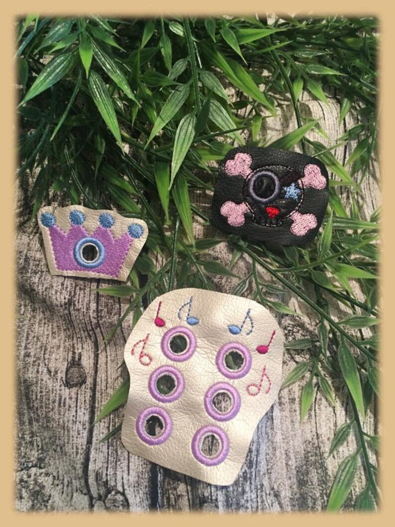 May include: Three felt patches with embroidered designs. A purple crown with blue accents, a black skull with pink accents, and a gold skull with purple accents and musical notes.