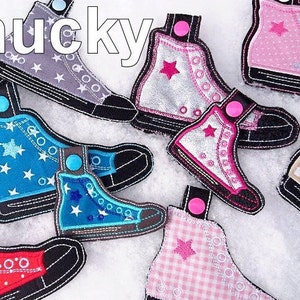 May include: A collection of colorful embroidered felt shoe charms with star patterns. The charms are in various colors, including pink, blue, gray, and silver. The charms are all in the shape of a high-top sneaker with laces and a star on the side. The word "Chucky" is written in white letters at the top of the image.