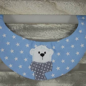 May include: A light blue baby bib with white stars and a white polar bear with a gray and white scarf.