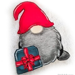 Può includere: Un gnomo grigio e rosso che tiene una scatola regalo blu con un fiocco rosso. Il gnomo ha un cappello rosso con un bordo bianco e una barba bianca.