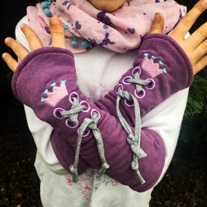 May include: Purple arm warmers with a gray lace-up detail and a pink crown embroidered on each warmer.