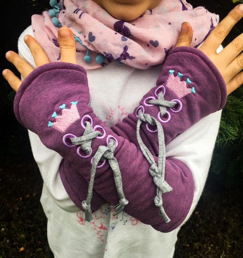 May include: Purple arm warmers with a gray lace-up detail and a pink crown embroidered on each warmer.