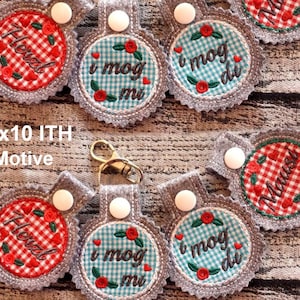 May include: Seven embroidered keychains with different designs. The keychains are gray with white buttons and feature red and blue checkered patterns with embroidered text. The text on the keychains includes "I mog di", "I mog mi", and "Herz".