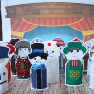 Puede incluir: Un conjunto de diez títeres de dedo que representan diferentes profesiones. Los títeres están hechos de fieltro y tienen detalles bordados. Los títeres están dispuestos en una fila sobre una superficie de madera. El letrero sobre los títeres dice "Herzlich willkommen in diesem Theater".