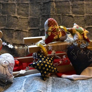 Könnte beinhalten: Ein Holzschlitten gefüllt mit handgefertigten Stoffschmuck. Der Schmuck ist in Form von Herzen und Sternen und mit verschiedenen Mustern und Stickereien verziert. Der Schmuck ist in Rot, Blau, Gold und Weiß.