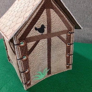 May include: A brown and tan felt birdhouse with a black bird silhouette on the front. The birdhouse has a green felt plant on the bottom and brown felt trim around the edges. The birdhouse is sitting on a green felt surface.