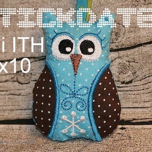 May include: A blue and brown owl-shaped plush toy with white polka dots and embroidered details. The toy is 10 inches by 10 inches and has a snowflake design on the front.