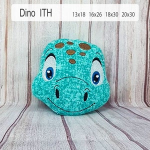 May include: A turquoise blue dinosaur plush toy with brown spots and white eyes. The toy is smiling and has a textured surface.