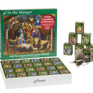 May include: A 1000 piece jigsaw puzzle advent calendar with a Christmas nativity scene. The box is green and features the words "In the Manger" and "24 Day Countdown to Christmas!" The puzzle pieces are arranged in a grid of 24 squares, each with a different number from 1 to 24. The puzzle pieces are green and have a Christmas tree design.