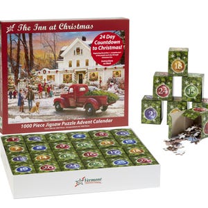 May include: A 1000 piece jigsaw puzzle advent calendar featuring a winter scene of a red truck with a Christmas tree in front of a house with the words "The Inn at Christmas" and "24 Day Countdown to Christmas!" on the box. The puzzle pieces are arranged in a grid of 24 squares, each with a number from 1 to 24.